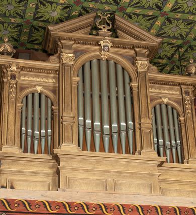 Zdjęcie nr 1: Organy architektoniczne, trójosiowe, na podwójnym cokole. Osie wydzielone pilastrami dźwigającymi gzyms z kostkowaniem. Środkowa wyższa niż boczne, zwieńczona trójkątnym, przerwanym przyczółkiem; pośrodku na gzymsie, rzeźbiona lira na cokole. Na osiach prześwity na piszczałki w formie stojącego prostokąta zamkniętego łukiem półkolistym, flankowanym przez półpilastry podtrzymujące profilowaną archiwoltę zwieńczoną kluczem; w osiach bocznych klucz w postaci liścia, w środkowej kartusz z głową. Zewnętrzne pilastry dekorowane kaboszonami i kampanulami, na gzymsie osi bocznych wazony. Struktura bejcowana w kolorze brązowym, ornamentyka złocona.