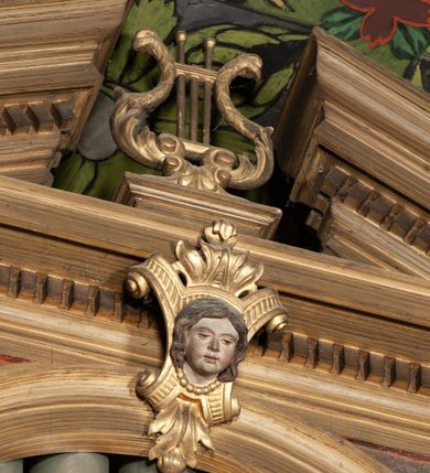 Zdjęcie nr 5: Organy architektoniczne, trójosiowe, na podwójnym cokole. Osie wydzielone pilastrami dźwigającymi gzyms z kostkowaniem. Środkowa wyższa niż boczne, zwieńczona trójkątnym, przerwanym przyczółkiem; pośrodku na gzymsie, rzeźbiona lira na cokole. Na osiach prześwity na piszczałki w formie stojącego prostokąta zamkniętego łukiem półkolistym, flankowanym przez półpilastry podtrzymujące profilowaną archiwoltę zwieńczoną kluczem; w osiach bocznych klucz w postaci liścia, w środkowej kartusz z głową. Zewnętrzne pilastry dekorowane kaboszonami i kampanulami, na gzymsie osi bocznych wazony. Struktura bejcowana w kolorze brązowym, ornamentyka złocona.