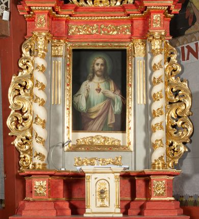 Zdjęcie nr 1: Ołtarz architektoniczny, jednokondygnacyjny, jednoosiowy, ze zwieńczeniem i drewnianą, sarkofagową mensą z kamiennym portatylem. Na mensie ołtarza kremowe tabernakulum w formie prostopadłościennej szafki, ujęte parą korynckich, złoconych półkolumienek, stojących na wyłamującym się, zdwojonym cokoliku, wspierających silnie wysunięty gzyms wieńczący. Drzwiczki w kształcie stojącego prostokąta, z prostokątną płyciną zwieńczoną łukiem półkolistym, zdobioną płaskorzeźbionym motywem kielicha, hostii, kłosów zboża i winnych gron.  Retabulum na cokole, ujęte parą pilastrów korynckich, z kanelurowaniem do połowy trzonu i parą filarów na tle których ustawiona jest para kolumn akantowych o spiralnie skręconych trzonach. Podpory wspierają wyłamujące się ponad nimi belkowanie o wysuniętym gzymsie. Zwieńczenie w formie stojącego owalu ujętego ażurową, akantową ramą, flankowane przerwanym, wklęsło wypukłym przyczółkiem. Dolne naroża antepedium zdobione motywem lwiej łapy ujętej parą wolut, z liściem akantu w zwieńczeniu. Pola cokołu, dolna partia pola środkowego i pola wewnątrz wnęki oraz fryz retabulum zdobiony motywem wici akantowej. Na trzonach kolumn retabulum spiralnie oplatająca je wić roślinna. Część środkowa retabulum ujęta parą ażurowych, akantowych uszaków. Pole środkowe w formie wnęki w kształcie stojącego prostokąta z przedstawieniem Najświętszego Serca Jezusa (druk) i obrazem św. Józefa (XX w.) na zasuwie. W zwieńczeniu pole obrazowe w kształcie stojącego owalu z przedstawieniem św. Jana Nepomucena. Na gzymsie przyczółka para siedzących aniołków. Kolorystyka struktury ołtarza w odcieniach szarości i czerwieni; ornamentyka i fragmenty detali architektonicznych złocone.  