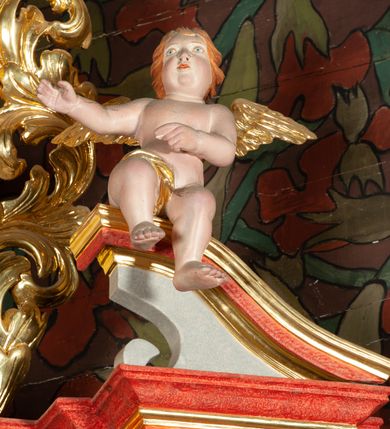 Zdjęcie nr 8: Ołtarz architektoniczny, jednokondygnacyjny, jednoosiowy, ze zwieńczeniem i drewnianą, sarkofagową mensą z kamiennym portatylem. Na mensie ołtarza kremowe tabernakulum w formie prostopadłościennej szafki, ujęte parą korynckich, złoconych półkolumienek, stojących na wyłamującym się, zdwojonym cokoliku, wspierających silnie wysunięty gzyms wieńczący. Drzwiczki w kształcie stojącego prostokąta, z prostokątną płyciną zwieńczoną łukiem półkolistym, zdobioną płaskorzeźbionym motywem kielicha, hostii, kłosów zboża i winnych gron.  Retabulum na cokole, ujęte parą pilastrów korynckich, z kanelurowaniem do połowy trzonu i parą filarów na tle których ustawiona jest para kolumn akantowych o spiralnie skręconych trzonach. Podpory wspierają wyłamujące się ponad nimi belkowanie o wysuniętym gzymsie. Zwieńczenie w formie stojącego owalu ujętego ażurową, akantową ramą, flankowane przerwanym, wklęsło wypukłym przyczółkiem. Dolne naroża antepedium zdobione motywem lwiej łapy ujętej parą wolut, z liściem akantu w zwieńczeniu. Pola cokołu, dolna partia pola środkowego i pola wewnątrz wnęki oraz fryz retabulum zdobiony motywem wici akantowej. Na trzonach kolumn retabulum spiralnie oplatająca je wić roślinna. Część środkowa retabulum ujęta parą ażurowych, akantowych uszaków. Pole środkowe w formie wnęki w kształcie stojącego prostokąta z przedstawieniem Najświętszego Serca Jezusa (druk) i obrazem św. Józefa (XX w.) na zasuwie. W zwieńczeniu pole obrazowe w kształcie stojącego owalu z przedstawieniem św. Jana Nepomucena. Na gzymsie przyczółka para siedzących aniołków. Kolorystyka struktury ołtarza w odcieniach szarości i czerwieni; ornamentyka i fragmenty detali architektonicznych złocone.  