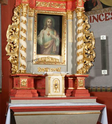 Zdjęcie nr 3: Ołtarz architektoniczny, jednokondygnacyjny, jednoosiowy, ze zwieńczeniem i drewnianą, sarkofagową mensą z kamiennym portatylem. Na mensie ołtarza kremowe tabernakulum w formie prostopadłościennej szafki, ujęte parą korynckich, złoconych półkolumienek, stojących na wyłamującym się, zdwojonym cokoliku, wspierających silnie wysunięty gzyms wieńczący. Drzwiczki w kształcie stojącego prostokąta, z prostokątną płyciną zwieńczoną łukiem półkolistym, zdobioną płaskorzeźbionym motywem kielicha, hostii, kłosów zboża i winnych gron.  Retabulum na cokole, ujęte parą pilastrów korynckich, z kanelurowaniem do połowy trzonu i parą filarów na tle których ustawiona jest para kolumn akantowych o spiralnie skręconych trzonach. Podpory wspierają wyłamujące się ponad nimi belkowanie o wysuniętym gzymsie. Zwieńczenie w formie stojącego owalu ujętego ażurową, akantową ramą, flankowane przerwanym, wklęsło wypukłym przyczółkiem. Dolne naroża antepedium zdobione motywem lwiej łapy ujętej parą wolut, z liściem akantu w zwieńczeniu. Pola cokołu, dolna partia pola środkowego i pola wewnątrz wnęki oraz fryz retabulum zdobiony motywem wici akantowej. Na trzonach kolumn retabulum spiralnie oplatająca je wić roślinna. Część środkowa retabulum ujęta parą ażurowych, akantowych uszaków. Pole środkowe w formie wnęki w kształcie stojącego prostokąta z przedstawieniem Najświętszego Serca Jezusa (druk) i obrazem św. Józefa (XX w.) na zasuwie. W zwieńczeniu pole obrazowe w kształcie stojącego owalu z przedstawieniem św. Jana Nepomucena. Na gzymsie przyczółka para siedzących aniołków. Kolorystyka struktury ołtarza w odcieniach szarości i czerwieni; ornamentyka i fragmenty detali architektonicznych złocone.  