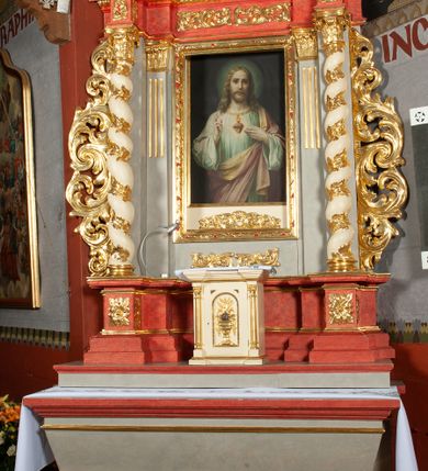 Zdjęcie nr 2: Ołtarz architektoniczny, jednokondygnacyjny, jednoosiowy, ze zwieńczeniem i drewnianą, sarkofagową mensą z kamiennym portatylem. Na mensie ołtarza kremowe tabernakulum w formie prostopadłościennej szafki, ujęte parą korynckich, złoconych półkolumienek, stojących na wyłamującym się, zdwojonym cokoliku, wspierających silnie wysunięty gzyms wieńczący. Drzwiczki w kształcie stojącego prostokąta, z prostokątną płyciną zwieńczoną łukiem półkolistym, zdobioną płaskorzeźbionym motywem kielicha, hostii, kłosów zboża i winnych gron.  Retabulum na cokole, ujęte parą pilastrów korynckich, z kanelurowaniem do połowy trzonu i parą filarów na tle których ustawiona jest para kolumn akantowych o spiralnie skręconych trzonach. Podpory wspierają wyłamujące się ponad nimi belkowanie o wysuniętym gzymsie. Zwieńczenie w formie stojącego owalu ujętego ażurową, akantową ramą, flankowane przerwanym, wklęsło wypukłym przyczółkiem. Dolne naroża antepedium zdobione motywem lwiej łapy ujętej parą wolut, z liściem akantu w zwieńczeniu. Pola cokołu, dolna partia pola środkowego i pola wewnątrz wnęki oraz fryz retabulum zdobiony motywem wici akantowej. Na trzonach kolumn retabulum spiralnie oplatająca je wić roślinna. Część środkowa retabulum ujęta parą ażurowych, akantowych uszaków. Pole środkowe w formie wnęki w kształcie stojącego prostokąta z przedstawieniem Najświętszego Serca Jezusa (druk) i obrazem św. Józefa (XX w.) na zasuwie. W zwieńczeniu pole obrazowe w kształcie stojącego owalu z przedstawieniem św. Jana Nepomucena. Na gzymsie przyczółka para siedzących aniołków. Kolorystyka struktury ołtarza w odcieniach szarości i czerwieni; ornamentyka i fragmenty detali architektonicznych złocone.  