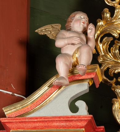 Zdjęcie nr 7: Ołtarz architektoniczny, jednokondygnacyjny, jednoosiowy, ze zwieńczeniem i drewnianą, sarkofagową mensą z kamiennym portatylem. Na mensie ołtarza kremowe tabernakulum w formie prostopadłościennej szafki, ujęte parą korynckich, złoconych półkolumienek, stojących na wyłamującym się, zdwojonym cokoliku, wspierających silnie wysunięty gzyms wieńczący. Drzwiczki w kształcie stojącego prostokąta, z prostokątną płyciną zwieńczoną łukiem półkolistym, zdobioną płaskorzeźbionym motywem kielicha, hostii, kłosów zboża i winnych gron.  Retabulum na cokole, ujęte parą pilastrów korynckich, z kanelurowaniem do połowy trzonu i parą filarów na tle których ustawiona jest para kolumn akantowych o spiralnie skręconych trzonach. Podpory wspierają wyłamujące się ponad nimi belkowanie o wysuniętym gzymsie. Zwieńczenie w formie stojącego owalu ujętego ażurową, akantową ramą, flankowane przerwanym, wklęsło wypukłym przyczółkiem. Dolne naroża antepedium zdobione motywem lwiej łapy ujętej parą wolut, z liściem akantu w zwieńczeniu. Pola cokołu, dolna partia pola środkowego i pola wewnątrz wnęki oraz fryz retabulum zdobiony motywem wici akantowej. Na trzonach kolumn retabulum spiralnie oplatająca je wić roślinna. Część środkowa retabulum ujęta parą ażurowych, akantowych uszaków. Pole środkowe w formie wnęki w kształcie stojącego prostokąta z przedstawieniem Najświętszego Serca Jezusa (druk) i obrazem św. Józefa (XX w.) na zasuwie. W zwieńczeniu pole obrazowe w kształcie stojącego owalu z przedstawieniem św. Jana Nepomucena. Na gzymsie przyczółka para siedzących aniołków. Kolorystyka struktury ołtarza w odcieniach szarości i czerwieni; ornamentyka i fragmenty detali architektonicznych złocone.  