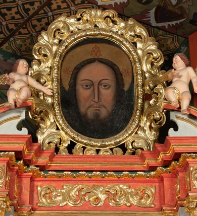 Zdjęcie nr 11: Ołtarz architektoniczny, jednokondygnacyjny, jednoosiowy, ze zwieńczeniem i drewnianą, sarkofagową mensą z kamiennym portatylem. Na mensie ołtarza kremowe tabernakulum w formie prostopadłościennej szafki, ujęte parą korynckich, złoconych półkolumienek, stojących na wyłamującym się, zdwojonym cokoliku, wspierających silnie wysunięty gzyms wieńczący. Drzwiczki w kształcie stojącego prostokąta, z prostokątną płyciną zwieńczoną łukiem półkolistym, zdobioną płaskorzeźbionym motywem kielicha, hostii, kłosów zboża i winnych gron.  Retabulum na cokole, ujęte parą pilastrów korynckich, z kanelurowaniem do połowy trzonu i parą filarów, na tle których ustawiona jest para kolumn akantowych o spiralnie skręconych trzonach. Podpory wspierają wyłamujące się ponad nimi belkowanie o wysuniętym gzymsie. Zwieńczenie w formie stojącego owalu ujętego ażurową, akantową ramą, flankowane przerwanym, wklęsło wypukłym przyczółkiem. Dolne naroża antepedium zdobione motywem lwiej łapy ujętej parą wolut, z liściem akantu w zwieńczeniu. Pola cokołu, dolna partia pola środkowego i pola wewnątrz wnęki, oraz fryz retabulum zdobiony motywem wici akantowej. Na trzonach kolumn retabulum spiralnie oplatająca ją wić roślinna. Cześć środkowa retabulum ujęta parą ażurowych, akantowych uszaków. Pole środkowe w formie wnęki w kształcie stojącego prostokąta z przedstawieniem Matki Boskiej Nieustającej Pomocy oraz Niepokalanego Poczęcia Najświętszej Marii Panny na zasuwie. W zwieńczeniu pole obrazowe w kształcie stojącego owalu z przedstawieniem Veraicon. Na gzymsie przyczółka para siedzących aniołków. Kolorystyka struktury ołtarza w odcieniach szarości i czerwieni; ornamentyka i fragmenty detali architektonicznych złocone.  