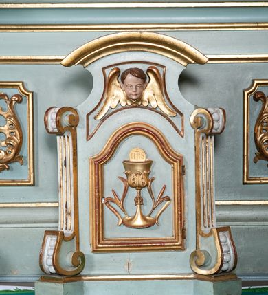 Zdjęcie nr 12: Nastawa architektoniczna, jednoosiowa, jednokondygnacyjna ze zwieńczeniem. Ołtarz drewniany, prostopadłościenny, z drewnianą mensą, ustawiony na profilowanym cokole. Ścianka frontowa ujęta pilastrami z płycinami w partii trzonów z akantem. W polu dwie płyciny o fantazyjnej formie wypełnione stylizowanym ornamentem akantowym, flankujące medalion z inicjałami „MS”. Ścianki boczne dekorowane płycinami. 
Na ołtarzu ustawione tabernakulum w formie drewnianej skrzynki, na cokole, flankowanej spływami wolutowymi, zwieńczonej szczytem zamkniętym łukowatym fragmentem gzymsu z płyciną i uskrzydloną główką anielską w polu. Drzwiczki w kształciestojącego prostokąta zamkniętego łukiem falistym, ujęte profilowaną ramą z przedstawieniem kielicha z hostią. 
Nastawa na cokole z wyodrębnionymi dwoma prostopadłościanami i dwoma skrajnymi konsolami, dekorowanym płycinami ze stylizowanym ornamentem. Retabulum ujęte parą kolumn o trzonach kanelowanych w jednej trzeciej wysokości, podtrzymujących belkowanie o architrawie i fryzie przerwanym nad polem środkowym. Na belkowaniu fragmenty przerwanego, półkolistego przyczółka z siedzącymi puttami. Niemal całe pole główne wypełnione wnęką w formie stojącego prostokąta zamkniętego łukiem półkolistym nadwieszonym, z uskokiem, w profilowanej ramie, z obrazami komunii anielskiej św. Stanisława Kostki i św. Józefa na zasuwie. Na konsolach, po bokach nastawy ustawione figury św. Wojciecha i św. Stanisława. Zwieńczenie w formie zbliżonej do stojącego prostokąta, ujętego spływami wolutowymi, zamkniętego dwiema stykającymi się wolutami oraz dwiema uskrzydlonymi główkami anielskimi w glorii promienistej. W polu obraz św. Rozalii w kształcie zbliżonym do zwieńczenia, ujęty profilowaną ramą. Struktura polichromowana w kolorze seledynowym, kolumny, profile i ornamentyka złocone. 


