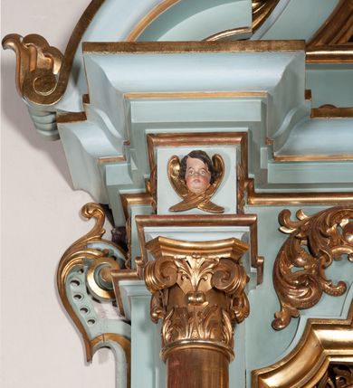 Zdjęcie nr 9: Nastawa architektoniczna, jednoosiowa, jednokondygnacyjna ze zwieńczeniem. Ołtarz drewniany, prostopadłościenny, z drewnianą mensą, ustawiony na profilowanym cokole. Ścianka frontowa ujęta pilastrami z płycinami w partii trzonów z akantem. W polu dwie płyciny o fantazyjnej formie wypełnione stylizowanym ornamentem akantowym, flankujące medalion z inicjałami „MS”. Ścianki boczne dekorowane płycinami. 
Na ołtarzu ustawione tabernakulum w formie drewnianej skrzynki, na cokole, flankowanej spływami wolutowymi, zwieńczonej szczytem zamkniętym łukowatym fragmentem gzymsu z płyciną i uskrzydloną główką anielską w polu. Drzwiczki w kształciestojącego prostokąta zamkniętego łukiem falistym, ujęte profilowaną ramą z przedstawieniem kielicha z hostią. 
Nastawa na cokole z wyodrębnionymi dwoma prostopadłościanami i dwoma skrajnymi konsolami, dekorowanym płycinami ze stylizowanym ornamentem. Retabulum ujęte parą kolumn o trzonach kanelowanych w jednej trzeciej wysokości, podtrzymujących belkowanie o architrawie i fryzie przerwanym nad polem środkowym. Na belkowaniu fragmenty przerwanego, półkolistego przyczółka z siedzącymi puttami. Niemal całe pole główne wypełnione wnęką w formie stojącego prostokąta zamkniętego łukiem półkolistym nadwieszonym, z uskokiem, w profilowanej ramie, z obrazami komunii anielskiej św. Stanisława Kostki i św. Józefa na zasuwie. Na konsolach, po bokach nastawy ustawione figury św. Wojciecha i św. Stanisława. Zwieńczenie w formie zbliżonej do stojącego prostokąta, ujętego spływami wolutowymi, zamkniętego dwiema stykającymi się wolutami oraz dwiema uskrzydlonymi główkami anielskimi w glorii promienistej. W polu obraz św. Rozalii w kształcie zbliżonym do zwieńczenia, ujęty profilowaną ramą. Struktura polichromowana w kolorze seledynowym, kolumny, profile i ornamentyka złocone. 


