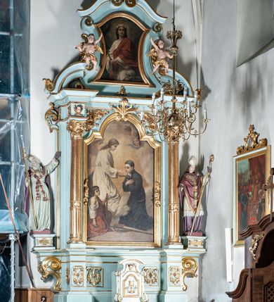 Zdjęcie nr 2: Nastawa architektoniczna, jednoosiowa, jednokondygnacyjna ze zwieńczeniem. Ołtarz drewniany, prostopadłościenny, z drewnianą mensą, ustawiony na profilowanym cokole. Ścianka frontowa ujęta pilastrami z płycinami w partii trzonów z akantem. W polu dwie płyciny o fantazyjnej formie wypełnione stylizowanym ornamentem akantowym, flankujące medalion z inicjałami „MS”. Ścianki boczne dekorowane płycinami. 
Na ołtarzu ustawione tabernakulum w formie drewnianej skrzynki, na cokole, flankowanej spływami wolutowymi, zwieńczonej szczytem zamkniętym łukowatym fragmentem gzymsu z płyciną i uskrzydloną główką anielską w polu. Drzwiczki w kształciestojącego prostokąta zamkniętego łukiem falistym, ujęte profilowaną ramą z przedstawieniem kielicha z hostią. 
Nastawa na cokole z wyodrębnionymi dwoma prostopadłościanami i dwoma skrajnymi konsolami, dekorowanym płycinami ze stylizowanym ornamentem. Retabulum ujęte parą kolumn o trzonach kanelowanych w jednej trzeciej wysokości, podtrzymujących belkowanie o architrawie i fryzie przerwanym nad polem środkowym. Na belkowaniu fragmenty przerwanego, półkolistego przyczółka z siedzącymi puttami. Niemal całe pole główne wypełnione wnęką w formie stojącego prostokąta zamkniętego łukiem półkolistym nadwieszonym, z uskokiem, w profilowanej ramie, z obrazami komunii anielskiej św. Stanisława Kostki i św. Józefa na zasuwie. Na konsolach, po bokach nastawy ustawione figury św. Wojciecha i św. Stanisława. Zwieńczenie w formie zbliżonej do stojącego prostokąta, ujętego spływami wolutowymi, zamkniętego dwiema stykającymi się wolutami oraz dwiema uskrzydlonymi główkami anielskimi w glorii promienistej. W polu obraz św. Rozalii w kształcie zbliżonym do zwieńczenia, ujęty profilowaną ramą. Struktura polichromowana w kolorze seledynowym, kolumny, profile i ornamentyka złocone. 


