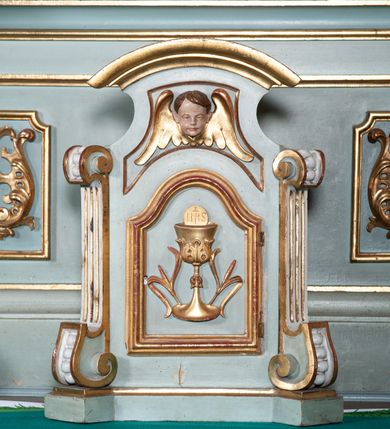 Zdjęcie nr 11: Nastawa architektoniczna, jednoosiowa, jednokondygnacyjna ze zwieńczeniem. Ołtarz drewniany, prostopadłościenny, z drewnianą mensą, ustawiony na profilowanym cokole. Ścianka frontowa ujęta pilastrami z płycinami w partii trzonów z akantem. W polu dwie płyciny o fantazyjnej formie wypełnione stylizowanym ornamentem akantowym, flankujące medalion z inicjałami „MS”. Ścianki boczne dekorowane płycinami. 
Na ołtarzu ustawione tabernakulum w formie drewnianej skrzynki, na cokole, flankowanej spływami wolutowymi, zwieńczonej szczytem zamkniętym łukowatym fragmentem gzymsu z płyciną i uskrzydloną główką anielską w polu. Drzwiczki w kształciestojącego prostokąta zamkniętego łukiem falistym, ujęte profilowaną ramą z przedstawieniem kielicha z hostią. 
Nastawa na cokole z wyodrębnionymi dwoma prostopadłościanami i dwoma skrajnymi konsolami, dekorowanym płycinami ze stylizowanym ornamentem. Retabulum ujęte parą kolumn o trzonach kanelowanych w jednej trzeciej wysokości, podtrzymujących belkowanie o architrawie i fryzie przerwanym nad polem środkowym. Na belkowaniu fragmenty przerwanego, półkolistego przyczółka z siedzącymi puttami. Niemal całe pole główne wypełnione wnęką w formie stojącego prostokąta zamkniętego łukiem półkolistym nadwieszonym, z uskokiem, w profilowanej ramie, z obrazami komunii anielskiej św. Stanisława Kostki i św. Józefa na zasuwie. Na konsolach, po bokach nastawy ustawione figury św. Wojciecha i św. Stanisława. Zwieńczenie w formie zbliżonej do stojącego prostokąta, ujętego spływami wolutowymi, zamkniętego dwiema stykającymi się wolutami oraz dwiema uskrzydlonymi główkami anielskimi w glorii promienistej. W polu obraz św. Rozalii w kształcie zbliżonym do zwieńczenia, ujęty profilowaną ramą. Struktura polichromowana w kolorze seledynowym, kolumny, profile i ornamentyka złocone. 


