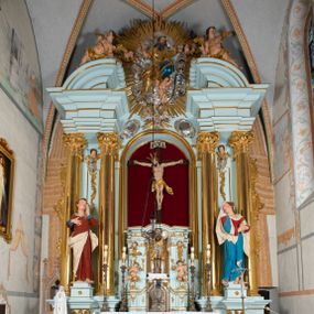 Zdjęcie nr 1: Nastawa architektoniczna, jednoosiowa, jednokondygnacyjna, ustawiona na wysokim cokole. 
Ołtarz drewniany, prostopadłościenny. Na nim tabernakulum z tronem wystawienia. Tabernakulum w formie drewnianej, prostopadłościennej skrzynki, obitej blachą, o wypukłej ściance frontowej, zamkniętej profilowanym gzymsem. Drzwiczki w formie stojącego prostokąta zamkniętego łukiem półkolistym, obwiedzione ramą, z wizerunkiem baranka z krzyżem, leżącego na księdze z pieczęciami, w glorii. Tabernakulum w drewnianej obudowie, wpisane w wysoki cokół, na nim tron wystawienia w formie obrotowej niszy w kształcie stojącego prostokąta, z podwieszoną draperią. Nisza flankowana parą pilastrów, przechodzących w spływy wolutowe, na których siedzą putta. Pilastry dźwigają pełne belkowanie, wyłamane na ich osi, częściowo przerwane przez niszę. Pilastry dekorowane uskrzydlonymi główkami anielskimi oraz snopkiem zboża i kiściami winogron. Cały tron wystawienia dekorowany rocaille&#039;m. 
Nastawa ujęta dwiema parami kolumn o kapitelach kompozytowych, dźwigających pełne belkowanie, wyłamane pomiędzy nimi, przerwane nad polem środkowym. Na belkowaniu fragmenty przerwanego, półkolistego przyczółka, na których leżą putta. Całe pole środkowe wypełnia wnęka w formie stojącego prostokąta zamkniętego łukiem półkolistym, ujęta profilowaną ramą, z figurą Chrystusa Ukrzyżowanego. Nad łukiem wnęki, pomiędzy obłokami, gołębica Ducha Świętego w glorii promienistej. Pomiędzy kolumnami płyciny z uskrzydlonymi główkami anielskimi na obłokach, rocaille oraz figury św.  Jana Ewangelisty i Matki Boskiej na rocaille&#039;owych wspornikach. Kondygnacja ujęta uszami utworzonymi z rocaille&#039;u. Nastawa zwieńczona rzeźbą tronującego Boga Ojca z globem i berłem, pośród obłoków i uskrzydlonych główek anielskich, w glorii promienistej. 
Struktura polichromowana w kolorze błękitnym, kolumny, profile i ornamentyka złocone. 
