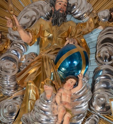 Zdjęcie nr 51: Nastawa architektoniczna, jednoosiowa, jednokondygnacyjna, ustawiona na wysokim cokole. 
Ołtarz drewniany, prostopadłościenny. Na nim tabernakulum z tronem wystawienia. Tabernakulum w formie drewnianej, prostopadłościennej skrzynki, obitej blachą, o wypukłej ściance frontowej, zamkniętej profilowanym gzymsem. Drzwiczki w formie stojącego prostokąta zamkniętego łukiem półkolistym, obwiedzione ramą, z wizerunkiem baranka z krzyżem, leżącego na księdze z pieczęciami, w glorii. Tabernakulum w drewnianej obudowie, wpisane w wysoki cokół, na nim tron wystawienia w formie obrotowej niszy w kształcie stojącego prostokąta, z podwieszoną draperią. Nisza flankowana parą pilastrów, przechodzących w spływy wolutowe, na których siedzą putta. Pilastry dźwigają pełne belkowanie, wyłamane na ich osi, częściowo przerwane przez niszę. Pilastry dekorowane uskrzydlonymi główkami anielskimi oraz snopkiem zboża i kiściami winogron. Cały tron wystawienia dekorowany rocaille'm. 
Nastawa ujęta dwiema parami kolumn o kapitelach kompozytowych, dźwigających pełne belkowanie, wyłamane pomiędzy nimi, przerwane nad polem środkowym. Na belkowaniu fragmenty przerwanego, półkolistego przyczółka, na których leżą putta. Całe pole środkowe wypełnia wnęka w formie stojącego prostokąta zamkniętego łukiem półkolistym, ujęta profilowaną ramą, z figurą Chrystusa Ukrzyżowanego. Nad łukiem wnęki, pomiędzy obłokami, gołębica Ducha Świętego w glorii promienistej. Pomiędzy kolumnami płyciny z uskrzydlonymi główkami anielskimi na obłokach, rocaille oraz figury św.  Jana Ewangelisty i Matki Boskiej na rocaille'owych wspornikach. Kondygnacja ujęta uszami utworzonymi z rocaille'u. Nastawa zwieńczona rzeźbą tronującego Boga Ojca z globem i berłem, pośród obłoków i uskrzydlonych główek anielskich, w glorii promienistej. 
Struktura polichromowana w kolorze błękitnym, kolumny, profile i ornamentyka złocone. 
