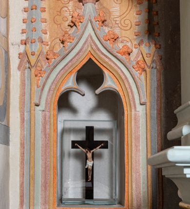 Zdjęcie nr 55: Nastawa architektoniczna, jednoosiowa, jednokondygnacyjna, ustawiona na wysokim cokole. 
Ołtarz drewniany, prostopadłościenny. Na nim tabernakulum z tronem wystawienia. Tabernakulum w formie drewnianej, prostopadłościennej skrzynki, obitej blachą, o wypukłej ściance frontowej, zamkniętej profilowanym gzymsem. Drzwiczki w formie stojącego prostokąta zamkniętego łukiem półkolistym, obwiedzione ramą, z wizerunkiem baranka z krzyżem, leżącego na księdze z pieczęciami, w glorii. Tabernakulum w drewnianej obudowie, wpisane w wysoki cokół, na nim tron wystawienia w formie obrotowej niszy w kształcie stojącego prostokąta, z podwieszoną draperią. Nisza flankowana parą pilastrów, przechodzących w spływy wolutowe, na których siedzą putta. Pilastry dźwigają pełne belkowanie, wyłamane na ich osi, częściowo przerwane przez niszę. Pilastry dekorowane uskrzydlonymi główkami anielskimi oraz snopkiem zboża i kiściami winogron. Cały tron wystawienia dekorowany rocaille'm. 
Nastawa ujęta dwiema parami kolumn o kapitelach kompozytowych, dźwigających pełne belkowanie, wyłamane pomiędzy nimi, przerwane nad polem środkowym. Na belkowaniu fragmenty przerwanego, półkolistego przyczółka, na których leżą putta. Całe pole środkowe wypełnia wnęka w formie stojącego prostokąta zamkniętego łukiem półkolistym, ujęta profilowaną ramą, z figurą Chrystusa Ukrzyżowanego. Nad łukiem wnęki, pomiędzy obłokami, gołębica Ducha Świętego w glorii promienistej. Pomiędzy kolumnami płyciny z uskrzydlonymi główkami anielskimi na obłokach, rocaille oraz figury św.  Jana Ewangelisty i Matki Boskiej na rocaille'owych wspornikach. Kondygnacja ujęta uszami utworzonymi z rocaille'u. Nastawa zwieńczona rzeźbą tronującego Boga Ojca z globem i berłem, pośród obłoków i uskrzydlonych główek anielskich, w glorii promienistej. 
Struktura polichromowana w kolorze błękitnym, kolumny, profile i ornamentyka złocone. 
