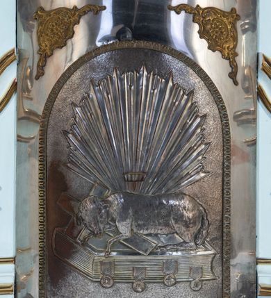 Zdjęcie nr 26: Nastawa architektoniczna, jednoosiowa, jednokondygnacyjna, ustawiona na wysokim cokole. 
Ołtarz drewniany, prostopadłościenny. Na nim tabernakulum z tronem wystawienia. Tabernakulum w formie drewnianej, prostopadłościennej skrzynki, obitej blachą, o wypukłej ściance frontowej, zamkniętej profilowanym gzymsem. Drzwiczki w formie stojącego prostokąta zamkniętego łukiem półkolistym, obwiedzione ramą, z wizerunkiem baranka z krzyżem, leżącego na księdze z pieczęciami, w glorii. Tabernakulum w drewnianej obudowie, wpisane w wysoki cokół, na nim tron wystawienia w formie obrotowej niszy w kształcie stojącego prostokąta, z podwieszoną draperią. Nisza flankowana parą pilastrów, przechodzących w spływy wolutowe, na których siedzą putta. Pilastry dźwigają pełne belkowanie, wyłamane na ich osi, częściowo przerwane przez niszę. Pilastry dekorowane uskrzydlonymi główkami anielskimi oraz snopkiem zboża i kiściami winogron. Cały tron wystawienia dekorowany rocaille'm. 
Nastawa ujęta dwiema parami kolumn o kapitelach kompozytowych, dźwigających pełne belkowanie, wyłamane pomiędzy nimi, przerwane nad polem środkowym. Na belkowaniu fragmenty przerwanego, półkolistego przyczółka, na których leżą putta. Całe pole środkowe wypełnia wnęka w formie stojącego prostokąta zamkniętego łukiem półkolistym, ujęta profilowaną ramą, z figurą Chrystusa Ukrzyżowanego. Nad łukiem wnęki, pomiędzy obłokami, gołębica Ducha Świętego w glorii promienistej. Pomiędzy kolumnami płyciny z uskrzydlonymi główkami anielskimi na obłokach, rocaille oraz figury św.  Jana Ewangelisty i Matki Boskiej na rocaille'owych wspornikach. Kondygnacja ujęta uszami utworzonymi z rocaille'u. Nastawa zwieńczona rzeźbą tronującego Boga Ojca z globem i berłem, pośród obłoków i uskrzydlonych główek anielskich, w glorii promienistej. 
Struktura polichromowana w kolorze błękitnym, kolumny, profile i ornamentyka złocone. 
