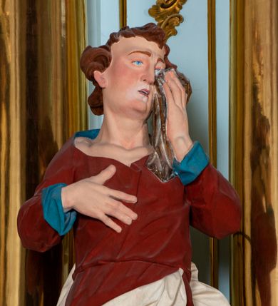 Zdjęcie nr 8: Nastawa architektoniczna, jednoosiowa, jednokondygnacyjna, ustawiona na wysokim cokole. 
Ołtarz drewniany, prostopadłościenny. Na nim tabernakulum z tronem wystawienia. Tabernakulum w formie drewnianej, prostopadłościennej skrzynki, obitej blachą, o wypukłej ściance frontowej, zamkniętej profilowanym gzymsem. Drzwiczki w formie stojącego prostokąta zamkniętego łukiem półkolistym, obwiedzione ramą, z wizerunkiem baranka z krzyżem, leżącego na księdze z pieczęciami, w glorii. Tabernakulum w drewnianej obudowie, wpisane w wysoki cokół, na nim tron wystawienia w formie obrotowej niszy w kształcie stojącego prostokąta, z podwieszoną draperią. Nisza flankowana parą pilastrów, przechodzących w spływy wolutowe, na których siedzą putta. Pilastry dźwigają pełne belkowanie, wyłamane na ich osi, częściowo przerwane przez niszę. Pilastry dekorowane uskrzydlonymi główkami anielskimi oraz snopkiem zboża i kiściami winogron. Cały tron wystawienia dekorowany rocaille&#039;m. 
Nastawa ujęta dwiema parami kolumn o kapitelach kompozytowych, dźwigających pełne belkowanie, wyłamane pomiędzy nimi, przerwane nad polem środkowym. Na belkowaniu fragmenty przerwanego, półkolistego przyczółka, na których leżą putta. Całe pole środkowe wypełnia wnęka w formie stojącego prostokąta zamkniętego łukiem półkolistym, ujęta profilowaną ramą, z figurą Chrystusa Ukrzyżowanego. Nad łukiem wnęki, pomiędzy obłokami, gołębica Ducha Świętego w glorii promienistej. Pomiędzy kolumnami płyciny z uskrzydlonymi główkami anielskimi na obłokach, rocaille oraz figury św.  Jana Ewangelisty i Matki Boskiej na rocaille&#039;owych wspornikach. Kondygnacja ujęta uszami utworzonymi z rocaille&#039;u. Nastawa zwieńczona rzeźbą tronującego Boga Ojca z globem i berłem, pośród obłoków i uskrzydlonych główek anielskich, w glorii promienistej. 
Struktura polichromowana w kolorze błękitnym, kolumny, profile i ornamentyka złocone. 
