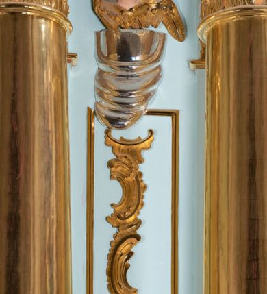 Zdjęcie nr 30: Nastawa architektoniczna, jednoosiowa, jednokondygnacyjna, ustawiona na wysokim cokole. 
Ołtarz drewniany, prostopadłościenny. Na nim tabernakulum z tronem wystawienia. Tabernakulum w formie drewnianej, prostopadłościennej skrzynki, obitej blachą, o wypukłej ściance frontowej, zamkniętej profilowanym gzymsem. Drzwiczki w formie stojącego prostokąta zamkniętego łukiem półkolistym, obwiedzione ramą, z wizerunkiem baranka z krzyżem, leżącego na księdze z pieczęciami, w glorii. Tabernakulum w drewnianej obudowie, wpisane w wysoki cokół, na nim tron wystawienia w formie obrotowej niszy w kształcie stojącego prostokąta, z podwieszoną draperią. Nisza flankowana parą pilastrów, przechodzących w spływy wolutowe, na których siedzą putta. Pilastry dźwigają pełne belkowanie, wyłamane na ich osi, częściowo przerwane przez niszę. Pilastry dekorowane uskrzydlonymi główkami anielskimi oraz snopkiem zboża i kiściami winogron. Cały tron wystawienia dekorowany rocaille'm. 
Nastawa ujęta dwiema parami kolumn o kapitelach kompozytowych, dźwigających pełne belkowanie, wyłamane pomiędzy nimi, przerwane nad polem środkowym. Na belkowaniu fragmenty przerwanego, półkolistego przyczółka, na których leżą putta. Całe pole środkowe wypełnia wnęka w formie stojącego prostokąta zamkniętego łukiem półkolistym, ujęta profilowaną ramą, z figurą Chrystusa Ukrzyżowanego. Nad łukiem wnęki, pomiędzy obłokami, gołębica Ducha Świętego w glorii promienistej. Pomiędzy kolumnami płyciny z uskrzydlonymi główkami anielskimi na obłokach, rocaille oraz figury św.  Jana Ewangelisty i Matki Boskiej na rocaille'owych wspornikach. Kondygnacja ujęta uszami utworzonymi z rocaille'u. Nastawa zwieńczona rzeźbą tronującego Boga Ojca z globem i berłem, pośród obłoków i uskrzydlonych główek anielskich, w glorii promienistej. 
Struktura polichromowana w kolorze błękitnym, kolumny, profile i ornamentyka złocone. 
