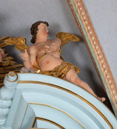 Zdjęcie nr 40: Nastawa architektoniczna, jednoosiowa, jednokondygnacyjna, ustawiona na wysokim cokole. 
Ołtarz drewniany, prostopadłościenny. Na nim tabernakulum z tronem wystawienia. Tabernakulum w formie drewnianej, prostopadłościennej skrzynki, obitej blachą, o wypukłej ściance frontowej, zamkniętej profilowanym gzymsem. Drzwiczki w formie stojącego prostokąta zamkniętego łukiem półkolistym, obwiedzione ramą, z wizerunkiem baranka z krzyżem, leżącego na księdze z pieczęciami, w glorii. Tabernakulum w drewnianej obudowie, wpisane w wysoki cokół, na nim tron wystawienia w formie obrotowej niszy w kształcie stojącego prostokąta, z podwieszoną draperią. Nisza flankowana parą pilastrów, przechodzących w spływy wolutowe, na których siedzą putta. Pilastry dźwigają pełne belkowanie, wyłamane na ich osi, częściowo przerwane przez niszę. Pilastry dekorowane uskrzydlonymi główkami anielskimi oraz snopkiem zboża i kiściami winogron. Cały tron wystawienia dekorowany rocaille&#039;m. 
Nastawa ujęta dwiema parami kolumn o kapitelach kompozytowych, dźwigających pełne belkowanie, wyłamane pomiędzy nimi, przerwane nad polem środkowym. Na belkowaniu fragmenty przerwanego, półkolistego przyczółka, na których leżą putta. Całe pole środkowe wypełnia wnęka w formie stojącego prostokąta zamkniętego łukiem półkolistym, ujęta profilowaną ramą, z figurą Chrystusa Ukrzyżowanego. Nad łukiem wnęki, pomiędzy obłokami, gołębica Ducha Świętego w glorii promienistej. Pomiędzy kolumnami płyciny z uskrzydlonymi główkami anielskimi na obłokach, rocaille oraz figury św.  Jana Ewangelisty i Matki Boskiej na rocaille&#039;owych wspornikach. Kondygnacja ujęta uszami utworzonymi z rocaille&#039;u. Nastawa zwieńczona rzeźbą tronującego Boga Ojca z globem i berłem, pośród obłoków i uskrzydlonych główek anielskich, w glorii promienistej. 
Struktura polichromowana w kolorze błękitnym, kolumny, profile i ornamentyka złocone. 
