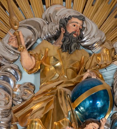 Zdjęcie nr 53: Nastawa architektoniczna, jednoosiowa, jednokondygnacyjna, ustawiona na wysokim cokole. 
Ołtarz drewniany, prostopadłościenny. Na nim tabernakulum z tronem wystawienia. Tabernakulum w formie drewnianej, prostopadłościennej skrzynki, obitej blachą, o wypukłej ściance frontowej, zamkniętej profilowanym gzymsem. Drzwiczki w formie stojącego prostokąta zamkniętego łukiem półkolistym, obwiedzione ramą, z wizerunkiem baranka z krzyżem, leżącego na księdze z pieczęciami, w glorii. Tabernakulum w drewnianej obudowie, wpisane w wysoki cokół, na nim tron wystawienia w formie obrotowej niszy w kształcie stojącego prostokąta, z podwieszoną draperią. Nisza flankowana parą pilastrów, przechodzących w spływy wolutowe, na których siedzą putta. Pilastry dźwigają pełne belkowanie, wyłamane na ich osi, częściowo przerwane przez niszę. Pilastry dekorowane uskrzydlonymi główkami anielskimi oraz snopkiem zboża i kiściami winogron. Cały tron wystawienia dekorowany rocaille'm. 
Nastawa ujęta dwiema parami kolumn o kapitelach kompozytowych, dźwigających pełne belkowanie, wyłamane pomiędzy nimi, przerwane nad polem środkowym. Na belkowaniu fragmenty przerwanego, półkolistego przyczółka, na których leżą putta. Całe pole środkowe wypełnia wnęka w formie stojącego prostokąta zamkniętego łukiem półkolistym, ujęta profilowaną ramą, z figurą Chrystusa Ukrzyżowanego. Nad łukiem wnęki, pomiędzy obłokami, gołębica Ducha Świętego w glorii promienistej. Pomiędzy kolumnami płyciny z uskrzydlonymi główkami anielskimi na obłokach, rocaille oraz figury św.  Jana Ewangelisty i Matki Boskiej na rocaille'owych wspornikach. Kondygnacja ujęta uszami utworzonymi z rocaille'u. Nastawa zwieńczona rzeźbą tronującego Boga Ojca z globem i berłem, pośród obłoków i uskrzydlonych główek anielskich, w glorii promienistej. 
Struktura polichromowana w kolorze błękitnym, kolumny, profile i ornamentyka złocone. 
