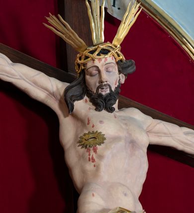 Zdjęcie nr 57: Nastawa architektoniczna, jednoosiowa, jednokondygnacyjna, ustawiona na wysokim cokole. 
Ołtarz drewniany, prostopadłościenny. Na nim tabernakulum z tronem wystawienia. Tabernakulum w formie drewnianej, prostopadłościennej skrzynki, obitej blachą, o wypukłej ściance frontowej, zamkniętej profilowanym gzymsem. Drzwiczki w formie stojącego prostokąta zamkniętego łukiem półkolistym, obwiedzione ramą, z wizerunkiem baranka z krzyżem, leżącego na księdze z pieczęciami, w glorii. Tabernakulum w drewnianej obudowie, wpisane w wysoki cokół, na nim tron wystawienia w formie obrotowej niszy w kształcie stojącego prostokąta, z podwieszoną draperią. Nisza flankowana parą pilastrów, przechodzących w spływy wolutowe, na których siedzą putta. Pilastry dźwigają pełne belkowanie, wyłamane na ich osi, częściowo przerwane przez niszę. Pilastry dekorowane uskrzydlonymi główkami anielskimi oraz snopkiem zboża i kiściami winogron. Cały tron wystawienia dekorowany rocaille'm. 
Nastawa ujęta dwiema parami kolumn o kapitelach kompozytowych, dźwigających pełne belkowanie, wyłamane pomiędzy nimi, przerwane nad polem środkowym. Na belkowaniu fragmenty przerwanego, półkolistego przyczółka, na których leżą putta. Całe pole środkowe wypełnia wnęka w formie stojącego prostokąta zamkniętego łukiem półkolistym, ujęta profilowaną ramą, z figurą Chrystusa Ukrzyżowanego. Nad łukiem wnęki, pomiędzy obłokami, gołębica Ducha Świętego w glorii promienistej. Pomiędzy kolumnami płyciny z uskrzydlonymi główkami anielskimi na obłokach, rocaille oraz figury św.  Jana Ewangelisty i Matki Boskiej na rocaille'owych wspornikach. Kondygnacja ujęta uszami utworzonymi z rocaille'u. Nastawa zwieńczona rzeźbą tronującego Boga Ojca z globem i berłem, pośród obłoków i uskrzydlonych główek anielskich, w glorii promienistej. 
Struktura polichromowana w kolorze błękitnym, kolumny, profile i ornamentyka złocone. 
