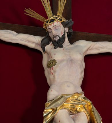 Zdjęcie nr 56: Nastawa architektoniczna, jednoosiowa, jednokondygnacyjna, ustawiona na wysokim cokole. 
Ołtarz drewniany, prostopadłościenny. Na nim tabernakulum z tronem wystawienia. Tabernakulum w formie drewnianej, prostopadłościennej skrzynki, obitej blachą, o wypukłej ściance frontowej, zamkniętej profilowanym gzymsem. Drzwiczki w formie stojącego prostokąta zamkniętego łukiem półkolistym, obwiedzione ramą, z wizerunkiem baranka z krzyżem, leżącego na księdze z pieczęciami, w glorii. Tabernakulum w drewnianej obudowie, wpisane w wysoki cokół, na nim tron wystawienia w formie obrotowej niszy w kształcie stojącego prostokąta, z podwieszoną draperią. Nisza flankowana parą pilastrów, przechodzących w spływy wolutowe, na których siedzą putta. Pilastry dźwigają pełne belkowanie, wyłamane na ich osi, częściowo przerwane przez niszę. Pilastry dekorowane uskrzydlonymi główkami anielskimi oraz snopkiem zboża i kiściami winogron. Cały tron wystawienia dekorowany rocaille'm. 
Nastawa ujęta dwiema parami kolumn o kapitelach kompozytowych, dźwigających pełne belkowanie, wyłamane pomiędzy nimi, przerwane nad polem środkowym. Na belkowaniu fragmenty przerwanego, półkolistego przyczółka, na których leżą putta. Całe pole środkowe wypełnia wnęka w formie stojącego prostokąta zamkniętego łukiem półkolistym, ujęta profilowaną ramą, z figurą Chrystusa Ukrzyżowanego. Nad łukiem wnęki, pomiędzy obłokami, gołębica Ducha Świętego w glorii promienistej. Pomiędzy kolumnami płyciny z uskrzydlonymi główkami anielskimi na obłokach, rocaille oraz figury św.  Jana Ewangelisty i Matki Boskiej na rocaille'owych wspornikach. Kondygnacja ujęta uszami utworzonymi z rocaille'u. Nastawa zwieńczona rzeźbą tronującego Boga Ojca z globem i berłem, pośród obłoków i uskrzydlonych główek anielskich, w glorii promienistej. 
Struktura polichromowana w kolorze błękitnym, kolumny, profile i ornamentyka złocone. 
