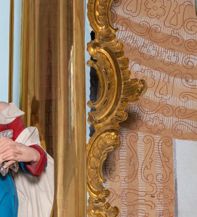 Zdjęcie nr 36: Nastawa architektoniczna, jednoosiowa, jednokondygnacyjna, ustawiona na wysokim cokole. 
Ołtarz drewniany, prostopadłościenny. Na nim tabernakulum z tronem wystawienia. Tabernakulum w formie drewnianej, prostopadłościennej skrzynki, obitej blachą, o wypukłej ściance frontowej, zamkniętej profilowanym gzymsem. Drzwiczki w formie stojącego prostokąta zamkniętego łukiem półkolistym, obwiedzione ramą, z wizerunkiem baranka z krzyżem, leżącego na księdze z pieczęciami, w glorii. Tabernakulum w drewnianej obudowie, wpisane w wysoki cokół, na nim tron wystawienia w formie obrotowej niszy w kształcie stojącego prostokąta, z podwieszoną draperią. Nisza flankowana parą pilastrów, przechodzących w spływy wolutowe, na których siedzą putta. Pilastry dźwigają pełne belkowanie, wyłamane na ich osi, częściowo przerwane przez niszę. Pilastry dekorowane uskrzydlonymi główkami anielskimi oraz snopkiem zboża i kiściami winogron. Cały tron wystawienia dekorowany rocaille&#039;m. 
Nastawa ujęta dwiema parami kolumn o kapitelach kompozytowych, dźwigających pełne belkowanie, wyłamane pomiędzy nimi, przerwane nad polem środkowym. Na belkowaniu fragmenty przerwanego, półkolistego przyczółka, na których leżą putta. Całe pole środkowe wypełnia wnęka w formie stojącego prostokąta zamkniętego łukiem półkolistym, ujęta profilowaną ramą, z figurą Chrystusa Ukrzyżowanego. Nad łukiem wnęki, pomiędzy obłokami, gołębica Ducha Świętego w glorii promienistej. Pomiędzy kolumnami płyciny z uskrzydlonymi główkami anielskimi na obłokach, rocaille oraz figury św.  Jana Ewangelisty i Matki Boskiej na rocaille&#039;owych wspornikach. Kondygnacja ujęta uszami utworzonymi z rocaille&#039;u. Nastawa zwieńczona rzeźbą tronującego Boga Ojca z globem i berłem, pośród obłoków i uskrzydlonych główek anielskich, w glorii promienistej. 
Struktura polichromowana w kolorze błękitnym, kolumny, profile i ornamentyka złocone. 
