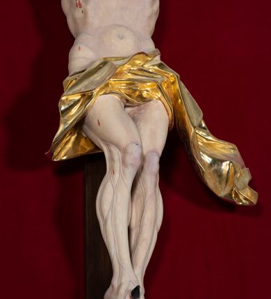 Zdjęcie nr 59: Nastawa architektoniczna, jednoosiowa, jednokondygnacyjna, ustawiona na wysokim cokole. 
Ołtarz drewniany, prostopadłościenny. Na nim tabernakulum z tronem wystawienia. Tabernakulum w formie drewnianej, prostopadłościennej skrzynki, obitej blachą, o wypukłej ściance frontowej, zamkniętej profilowanym gzymsem. Drzwiczki w formie stojącego prostokąta zamkniętego łukiem półkolistym, obwiedzione ramą, z wizerunkiem baranka z krzyżem, leżącego na księdze z pieczęciami, w glorii. Tabernakulum w drewnianej obudowie, wpisane w wysoki cokół, na nim tron wystawienia w formie obrotowej niszy w kształcie stojącego prostokąta, z podwieszoną draperią. Nisza flankowana parą pilastrów, przechodzących w spływy wolutowe, na których siedzą putta. Pilastry dźwigają pełne belkowanie, wyłamane na ich osi, częściowo przerwane przez niszę. Pilastry dekorowane uskrzydlonymi główkami anielskimi oraz snopkiem zboża i kiściami winogron. Cały tron wystawienia dekorowany rocaille&#039;m. 
Nastawa ujęta dwiema parami kolumn o kapitelach kompozytowych, dźwigających pełne belkowanie, wyłamane pomiędzy nimi, przerwane nad polem środkowym. Na belkowaniu fragmenty przerwanego, półkolistego przyczółka, na których leżą putta. Całe pole środkowe wypełnia wnęka w formie stojącego prostokąta zamkniętego łukiem półkolistym, ujęta profilowaną ramą, z figurą Chrystusa Ukrzyżowanego. Nad łukiem wnęki, pomiędzy obłokami, gołębica Ducha Świętego w glorii promienistej. Pomiędzy kolumnami płyciny z uskrzydlonymi główkami anielskimi na obłokach, rocaille oraz figury św.  Jana Ewangelisty i Matki Boskiej na rocaille&#039;owych wspornikach. Kondygnacja ujęta uszami utworzonymi z rocaille&#039;u. Nastawa zwieńczona rzeźbą tronującego Boga Ojca z globem i berłem, pośród obłoków i uskrzydlonych główek anielskich, w glorii promienistej. 
Struktura polichromowana w kolorze błękitnym, kolumny, profile i ornamentyka złocone. 
