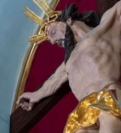 Zdjęcie nr 58: Nastawa architektoniczna, jednoosiowa, jednokondygnacyjna, ustawiona na wysokim cokole. 
Ołtarz drewniany, prostopadłościenny. Na nim tabernakulum z tronem wystawienia. Tabernakulum w formie drewnianej, prostopadłościennej skrzynki, obitej blachą, o wypukłej ściance frontowej, zamkniętej profilowanym gzymsem. Drzwiczki w formie stojącego prostokąta zamkniętego łukiem półkolistym, obwiedzione ramą, z wizerunkiem baranka z krzyżem, leżącego na księdze z pieczęciami, w glorii. Tabernakulum w drewnianej obudowie, wpisane w wysoki cokół, na nim tron wystawienia w formie obrotowej niszy w kształcie stojącego prostokąta, z podwieszoną draperią. Nisza flankowana parą pilastrów, przechodzących w spływy wolutowe, na których siedzą putta. Pilastry dźwigają pełne belkowanie, wyłamane na ich osi, częściowo przerwane przez niszę. Pilastry dekorowane uskrzydlonymi główkami anielskimi oraz snopkiem zboża i kiściami winogron. Cały tron wystawienia dekorowany rocaille&#039;m. 
Nastawa ujęta dwiema parami kolumn o kapitelach kompozytowych, dźwigających pełne belkowanie, wyłamane pomiędzy nimi, przerwane nad polem środkowym. Na belkowaniu fragmenty przerwanego, półkolistego przyczółka, na których leżą putta. Całe pole środkowe wypełnia wnęka w formie stojącego prostokąta zamkniętego łukiem półkolistym, ujęta profilowaną ramą, z figurą Chrystusa Ukrzyżowanego. Nad łukiem wnęki, pomiędzy obłokami, gołębica Ducha Świętego w glorii promienistej. Pomiędzy kolumnami płyciny z uskrzydlonymi główkami anielskimi na obłokach, rocaille oraz figury św.  Jana Ewangelisty i Matki Boskiej na rocaille&#039;owych wspornikach. Kondygnacja ujęta uszami utworzonymi z rocaille&#039;u. Nastawa zwieńczona rzeźbą tronującego Boga Ojca z globem i berłem, pośród obłoków i uskrzydlonych główek anielskich, w glorii promienistej. 
Struktura polichromowana w kolorze błękitnym, kolumny, profile i ornamentyka złocone. 
