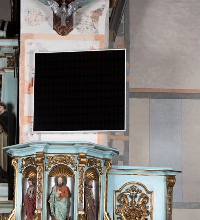 Zdjęcie nr 2: Kosz ambony na planie ośmioboku z szyszką i wolutami u podstawy. Ścianki kosza ujęte pilastrami z karbowaną wstęgą i kampanulami, zakończone od dołu wolutami z motywem liścia akantu oraz wolutą pod kapitelami. W czterech ścianach nisze ze złotymi konchami. W niszach rzeźby czterech ewangelistów z atrybutami. Ponad nimi motywy ornamentalne rocaille z różyczką pośrodku. Na zaplecku tablice Dekalogu na obłoku na tle glorii promienistej. Ujęte w prostokątną ramę zwieńczoną łukiem wklęsło-wypukłym. Baldachim ośmioboczny z podwieszoną glorią i gołębicą, fryz z motywami rocaille'ów i krzyży, wyłamany gzyms. W zwieńczeniu koncentrycznie schodzące się woluty. Ambona polichromowana na kolor seledynowy, detale złocone, postacie w różnobarwnych szatach, partie ciała potraktowane naturalistycznie. 