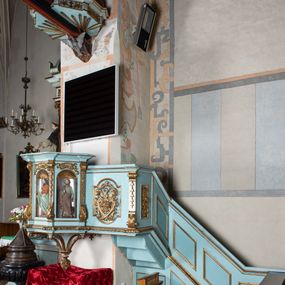 Zdjęcie nr 1: Kosz ambony na planie ośmioboku z szyszką i wolutami u podstawy. Ścianki kosza ujęte pilastrami z karbowaną wstęgą i kampanulami, zakończone od dołu wolutami z motywem liścia akantu oraz wolutą pod kapitelami. W czterech ścianach nisze ze złotymi konchami. W niszach rzeźby czterech ewangelistów z atrybutami. Ponad nimi motywy ornamentalne rocaille z różyczką pośrodku. Na zaplecku tablice Dekalogu na obłoku na tle glorii promienistej. Ujęte w prostokątną ramę zwieńczoną łukiem wklęsło-wypukłym. Baldachim ośmioboczny z podwieszoną glorią i gołębicą, fryz z motywami rocaille'ów i krzyży, wyłamany gzyms. W zwieńczeniu koncentrycznie schodzące się woluty. Ambona polichromowana na kolor seledynowy, detale złocone, postacie w różnobarwnych szatach, partie ciała potraktowane naturalistycznie. 