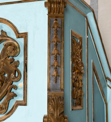 Zdjęcie nr 12: Kosz ambony na planie ośmioboku z szyszką i wolutami u podstawy. Ścianki kosza ujęte pilastrami z karbowaną wstęgą i kampanulami, zakończone od dołu wolutami z motywem liścia akantu oraz wolutą pod kapitelami. W czterech ścianach nisze ze złotymi konchami. W niszach rzeźby czterech ewangelistów z atrybutami. Ponad nimi motywy ornamentalne rocaille z różyczką pośrodku. Na zaplecku tablice Dekalogu na obłoku na tle glorii promienistej. Ujęte w prostokątną ramę zwieńczoną łukiem wklęsło-wypukłym. Baldachim ośmioboczny z podwieszoną glorią i gołębicą, fryz z motywami rocaille&#039;ów i krzyży, wyłamany gzyms. W zwieńczeniu koncentrycznie schodzące się woluty. Ambona polichromowana na kolor seledynowy, detale złocone, postacie w różnobarwnych szatach, partie ciała potraktowane naturalistycznie. 