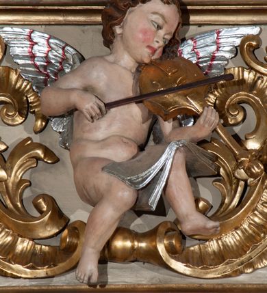 Zdjęcie nr 6: Parapet chóru muzycznego podtrzymywany przez dwie podpory. Balustrada na cokole, podzielona na cztery pola, wydzielone czterema pilastrami o trzonach w formie spływów wolutowych dekorowanych kampanulami i środkową hermą z półpostacią anioła. Pilastry podtrzymują niepełne belkowanie wyłamane na ich osi. Na belkowaniu, na osi skrajnych pilastrów wazony z kwiatami. W polach płyciny w formie leżącego prostokąta, ujęte profilowanymi ramami. W dwóch skrajnych płycinach przedstawienia instrumentów muzycznych ujętych rocaille&#039;m. Dwie środkowe płyciny z figurkami muzykujących puttów flankowanych rocaille&#039;m. Dolna krawędź balustrady, na osi środkowej dekorowana dwiema stykającymi się wolutami, przechodzącymi we wstęgę, ozdobioną rocaille&#039;m. Balustrada polichromowana w kolorze seledynowym, z kolorowymi profilami, ornamentyka i spływy wolutowe złocone i srebrzone. 


