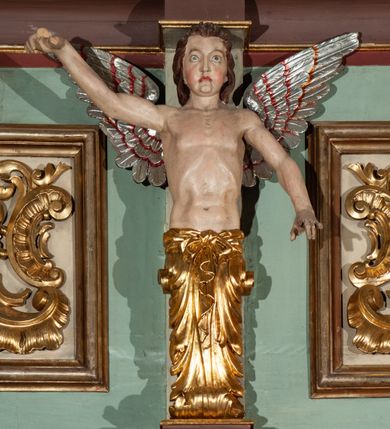 Zdjęcie nr 11: Parapet chóru muzycznego podtrzymywany przez dwie podpory. Balustrada na cokole, podzielona na cztery pola, wydzielone czterema pilastrami o trzonach w formie spływów wolutowych dekorowanych kampanulami i środkową hermą z półpostacią anioła. Pilastry podtrzymują niepełne belkowanie wyłamane na ich osi. Na belkowaniu, na osi skrajnych pilastrów wazony z kwiatami. W polach płyciny w formie leżącego prostokąta, ujęte profilowanymi ramami. W dwóch skrajnych płycinach przedstawienia instrumentów muzycznych ujętych rocaille'm. Dwie środkowe płyciny z figurkami muzykujących puttów flankowanych rocaille'm. Dolna krawędź balustrady, na osi środkowej dekorowana dwiema stykającymi się wolutami, przechodzącymi we wstęgę, ozdobioną rocaille'm. Balustrada polichromowana w kolorze seledynowym, z kolorowymi profilami, ornamentyka i spływy wolutowe złocone i srebrzone. 


