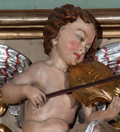 Zdjęcie nr 8: Parapet chóru muzycznego podtrzymywany przez dwie podpory. Balustrada na cokole, podzielona na cztery pola, wydzielone czterema pilastrami o trzonach w formie spływów wolutowych dekorowanych kampanulami i środkową hermą z półpostacią anioła. Pilastry podtrzymują niepełne belkowanie wyłamane na ich osi. Na belkowaniu, na osi skrajnych pilastrów wazony z kwiatami. W polach płyciny w formie leżącego prostokąta, ujęte profilowanymi ramami. W dwóch skrajnych płycinach przedstawienia instrumentów muzycznych ujętych rocaille&#039;m. Dwie środkowe płyciny z figurkami muzykujących puttów flankowanych rocaille&#039;m. Dolna krawędź balustrady, na osi środkowej dekorowana dwiema stykającymi się wolutami, przechodzącymi we wstęgę, ozdobioną rocaille&#039;m. Balustrada polichromowana w kolorze seledynowym, z kolorowymi profilami, ornamentyka i spływy wolutowe złocone i srebrzone. 


