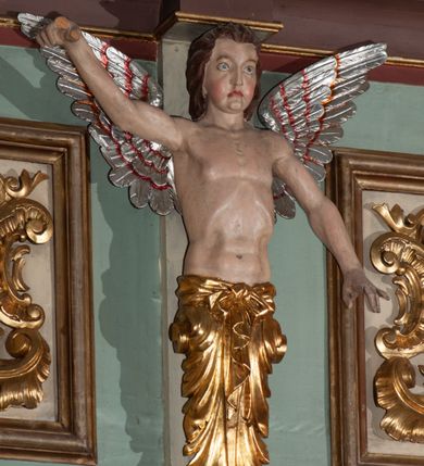 Zdjęcie nr 12: Parapet chóru muzycznego podtrzymywany przez dwie podpory. Balustrada na cokole, podzielona na cztery pola, wydzielone czterema pilastrami o trzonach w formie spływów wolutowych dekorowanych kampanulami i środkową hermą z półpostacią anioła. Pilastry podtrzymują niepełne belkowanie wyłamane na ich osi. Na belkowaniu, na osi skrajnych pilastrów wazony z kwiatami. W polach płyciny w formie leżącego prostokąta, ujęte profilowanymi ramami. W dwóch skrajnych płycinach przedstawienia instrumentów muzycznych ujętych rocaille'm. Dwie środkowe płyciny z figurkami muzykujących puttów flankowanych rocaille'm. Dolna krawędź balustrady, na osi środkowej dekorowana dwiema stykającymi się wolutami, przechodzącymi we wstęgę, ozdobioną rocaille'm. Balustrada polichromowana w kolorze seledynowym, z kolorowymi profilami, ornamentyka i spływy wolutowe złocone i srebrzone. 


