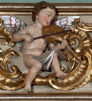 Zdjęcie nr 4: Parapet chóru muzycznego podtrzymywany przez dwie podpory. Balustrada na cokole, podzielona na cztery pola, wydzielone czterema pilastrami o trzonach w formie spływów wolutowych dekorowanych kampanulami i środkową hermą z półpostacią anioła. Pilastry podtrzymują niepełne belkowanie wyłamane na ich osi. Na belkowaniu, na osi skrajnych pilastrów wazony z kwiatami. W polach płyciny w formie leżącego prostokąta, ujęte profilowanymi ramami. W dwóch skrajnych płycinach przedstawienia instrumentów muzycznych ujętych rocaille'm. Dwie środkowe płyciny z figurkami muzykujących puttów flankowanych rocaille'm. Dolna krawędź balustrady, na osi środkowej dekorowana dwiema stykającymi się wolutami, przechodzącymi we wstęgę, ozdobioną rocaille'm. Balustrada polichromowana w kolorze seledynowym, z kolorowymi profilami, ornamentyka i spływy wolutowe złocone i srebrzone. 


