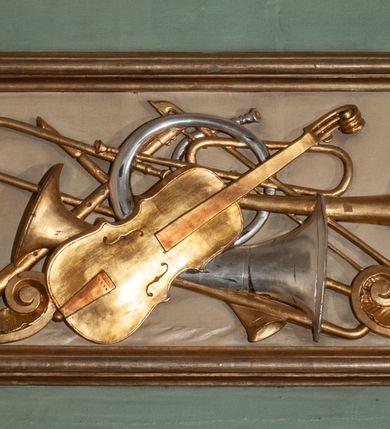 Zdjęcie nr 25: Parapet chóru muzycznego podtrzymywany przez dwie podpory. Balustrada na cokole, podzielona na cztery pola, wydzielone czterema pilastrami o trzonach w formie spływów wolutowych dekorowanych kampanulami i środkową hermą z półpostacią anioła. Pilastry podtrzymują niepełne belkowanie wyłamane na ich osi. Na belkowaniu, na osi skrajnych pilastrów wazony z kwiatami. W polach płyciny w formie leżącego prostokąta, ujęte profilowanymi ramami. W dwóch skrajnych płycinach przedstawienia instrumentów muzycznych ujętych rocaille&#039;m. Dwie środkowe płyciny z figurkami muzykujących puttów flankowanych rocaille&#039;m. Dolna krawędź balustrady, na osi środkowej dekorowana dwiema stykającymi się wolutami, przechodzącymi we wstęgę, ozdobioną rocaille&#039;m. Balustrada polichromowana w kolorze seledynowym, z kolorowymi profilami, ornamentyka i spływy wolutowe złocone i srebrzone. 


