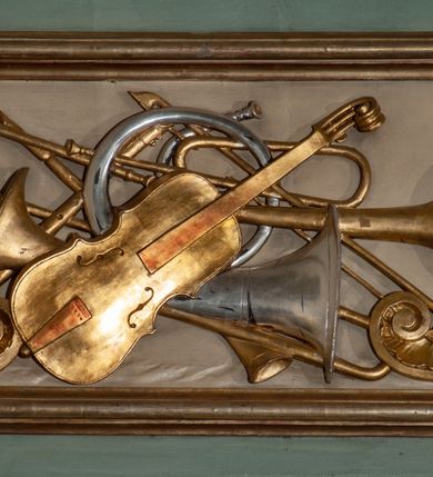 Zdjęcie nr 24: Parapet chóru muzycznego podtrzymywany przez dwie podpory. Balustrada na cokole, podzielona na cztery pola, wydzielone czterema pilastrami o trzonach w formie spływów wolutowych dekorowanych kampanulami i środkową hermą z półpostacią anioła. Pilastry podtrzymują niepełne belkowanie wyłamane na ich osi. Na belkowaniu, na osi skrajnych pilastrów wazony z kwiatami. W polach płyciny w formie leżącego prostokąta, ujęte profilowanymi ramami. W dwóch skrajnych płycinach przedstawienia instrumentów muzycznych ujętych rocaille&#039;m. Dwie środkowe płyciny z figurkami muzykujących puttów flankowanych rocaille&#039;m. Dolna krawędź balustrady, na osi środkowej dekorowana dwiema stykającymi się wolutami, przechodzącymi we wstęgę, ozdobioną rocaille&#039;m. Balustrada polichromowana w kolorze seledynowym, z kolorowymi profilami, ornamentyka i spływy wolutowe złocone i srebrzone. 


