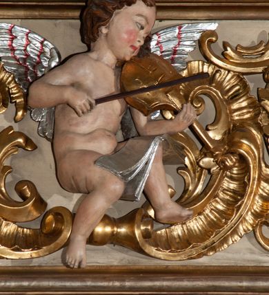 Zdjęcie nr 5: Parapet chóru muzycznego podtrzymywany przez dwie podpory. Balustrada na cokole, podzielona na cztery pola, wydzielone czterema pilastrami o trzonach w formie spływów wolutowych dekorowanych kampanulami i środkową hermą z półpostacią anioła. Pilastry podtrzymują niepełne belkowanie wyłamane na ich osi. Na belkowaniu, na osi skrajnych pilastrów wazony z kwiatami. W polach płyciny w formie leżącego prostokąta, ujęte profilowanymi ramami. W dwóch skrajnych płycinach przedstawienia instrumentów muzycznych ujętych rocaille&#039;m. Dwie środkowe płyciny z figurkami muzykujących puttów flankowanych rocaille&#039;m. Dolna krawędź balustrady, na osi środkowej dekorowana dwiema stykającymi się wolutami, przechodzącymi we wstęgę, ozdobioną rocaille&#039;m. Balustrada polichromowana w kolorze seledynowym, z kolorowymi profilami, ornamentyka i spływy wolutowe złocone i srebrzone. 


