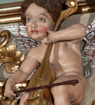 Zdjęcie nr 22: Parapet chóru muzycznego podtrzymywany przez dwie podpory. Balustrada na cokole, podzielona na cztery pola, wydzielone czterema pilastrami o trzonach w formie spływów wolutowych dekorowanych kampanulami i środkową hermą z półpostacią anioła. Pilastry podtrzymują niepełne belkowanie wyłamane na ich osi. Na belkowaniu, na osi skrajnych pilastrów wazony z kwiatami. W polach płyciny w formie leżącego prostokąta, ujęte profilowanymi ramami. W dwóch skrajnych płycinach przedstawienia instrumentów muzycznych ujętych rocaille&#039;m. Dwie środkowe płyciny z figurkami muzykujących puttów flankowanych rocaille&#039;m. Dolna krawędź balustrady, na osi środkowej dekorowana dwiema stykającymi się wolutami, przechodzącymi we wstęgę, ozdobioną rocaille&#039;m. Balustrada polichromowana w kolorze seledynowym, z kolorowymi profilami, ornamentyka i spływy wolutowe złocone i srebrzone. 


