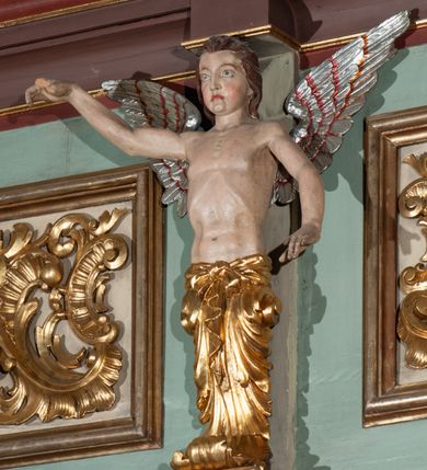 Zdjęcie nr 10: Parapet chóru muzycznego podtrzymywany przez dwie podpory. Balustrada na cokole, podzielona na cztery pola, wydzielone czterema pilastrami o trzonach w formie spływów wolutowych dekorowanych kampanulami i środkową hermą z półpostacią anioła. Pilastry podtrzymują niepełne belkowanie wyłamane na ich osi. Na belkowaniu, na osi skrajnych pilastrów wazony z kwiatami. W polach płyciny w formie leżącego prostokąta, ujęte profilowanymi ramami. W dwóch skrajnych płycinach przedstawienia instrumentów muzycznych ujętych rocaille'm. Dwie środkowe płyciny z figurkami muzykujących puttów flankowanych rocaille'm. Dolna krawędź balustrady, na osi środkowej dekorowana dwiema stykającymi się wolutami, przechodzącymi we wstęgę, ozdobioną rocaille'm. Balustrada polichromowana w kolorze seledynowym, z kolorowymi profilami, ornamentyka i spływy wolutowe złocone i srebrzone. 


