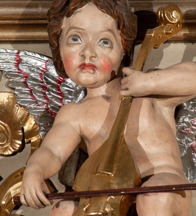 Zdjęcie nr 21: Parapet chóru muzycznego podtrzymywany przez dwie podpory. Balustrada na cokole, podzielona na cztery pola, wydzielone czterema pilastrami o trzonach w formie spływów wolutowych dekorowanych kampanulami i środkową hermą z półpostacią anioła. Pilastry podtrzymują niepełne belkowanie wyłamane na ich osi. Na belkowaniu, na osi skrajnych pilastrów wazony z kwiatami. W polach płyciny w formie leżącego prostokąta, ujęte profilowanymi ramami. W dwóch skrajnych płycinach przedstawienia instrumentów muzycznych ujętych rocaille'm. Dwie środkowe płyciny z figurkami muzykujących puttów flankowanych rocaille'm. Dolna krawędź balustrady, na osi środkowej dekorowana dwiema stykającymi się wolutami, przechodzącymi we wstęgę, ozdobioną rocaille'm. Balustrada polichromowana w kolorze seledynowym, z kolorowymi profilami, ornamentyka i spływy wolutowe złocone i srebrzone. 


