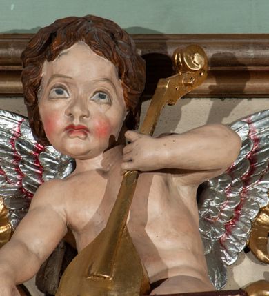 Zdjęcie nr 23: Parapet chóru muzycznego podtrzymywany przez dwie podpory. Balustrada na cokole, podzielona na cztery pola, wydzielone czterema pilastrami o trzonach w formie spływów wolutowych dekorowanych kampanulami i środkową hermą z półpostacią anioła. Pilastry podtrzymują niepełne belkowanie wyłamane na ich osi. Na belkowaniu, na osi skrajnych pilastrów wazony z kwiatami. W polach płyciny w formie leżącego prostokąta, ujęte profilowanymi ramami. W dwóch skrajnych płycinach przedstawienia instrumentów muzycznych ujętych rocaille&#039;m. Dwie środkowe płyciny z figurkami muzykujących puttów flankowanych rocaille&#039;m. Dolna krawędź balustrady, na osi środkowej dekorowana dwiema stykającymi się wolutami, przechodzącymi we wstęgę, ozdobioną rocaille&#039;m. Balustrada polichromowana w kolorze seledynowym, z kolorowymi profilami, ornamentyka i spływy wolutowe złocone i srebrzone. 


