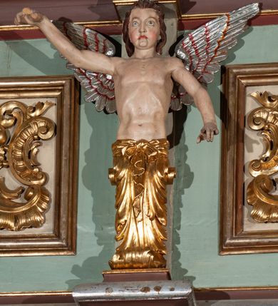 Zdjęcie nr 13: Parapet chóru muzycznego podtrzymywany przez dwie podpory. Balustrada na cokole, podzielona na cztery pola, wydzielone czterema pilastrami o trzonach w formie spływów wolutowych dekorowanych kampanulami i środkową hermą z półpostacią anioła. Pilastry podtrzymują niepełne belkowanie wyłamane na ich osi. Na belkowaniu, na osi skrajnych pilastrów wazony z kwiatami. W polach płyciny w formie leżącego prostokąta, ujęte profilowanymi ramami. W dwóch skrajnych płycinach przedstawienia instrumentów muzycznych ujętych rocaille'm. Dwie środkowe płyciny z figurkami muzykujących puttów flankowanych rocaille'm. Dolna krawędź balustrady, na osi środkowej dekorowana dwiema stykającymi się wolutami, przechodzącymi we wstęgę, ozdobioną rocaille'm. Balustrada polichromowana w kolorze seledynowym, z kolorowymi profilami, ornamentyka i spływy wolutowe złocone i srebrzone. 


