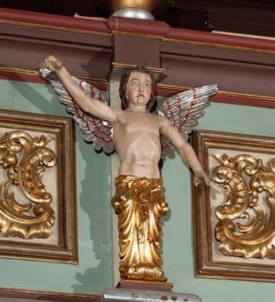 Zdjęcie nr 9: Parapet chóru muzycznego podtrzymywany przez dwie podpory. Balustrada na cokole, podzielona na cztery pola, wydzielone czterema pilastrami o trzonach w formie spływów wolutowych dekorowanych kampanulami i środkową hermą z półpostacią anioła. Pilastry podtrzymują niepełne belkowanie wyłamane na ich osi. Na belkowaniu, na osi skrajnych pilastrów wazony z kwiatami. W polach płyciny w formie leżącego prostokąta, ujęte profilowanymi ramami. W dwóch skrajnych płycinach przedstawienia instrumentów muzycznych ujętych rocaille'm. Dwie środkowe płyciny z figurkami muzykujących puttów flankowanych rocaille'm. Dolna krawędź balustrady, na osi środkowej dekorowana dwiema stykającymi się wolutami, przechodzącymi we wstęgę, ozdobioną rocaille'm. Balustrada polichromowana w kolorze seledynowym, z kolorowymi profilami, ornamentyka i spływy wolutowe złocone i srebrzone. 


