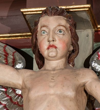 Zdjęcie nr 16: Parapet chóru muzycznego podtrzymywany przez dwie podpory. Balustrada na cokole, podzielona na cztery pola, wydzielone czterema pilastrami o trzonach w formie spływów wolutowych dekorowanych kampanulami i środkową hermą z półpostacią anioła. Pilastry podtrzymują niepełne belkowanie wyłamane na ich osi. Na belkowaniu, na osi skrajnych pilastrów wazony z kwiatami. W polach płyciny w formie leżącego prostokąta, ujęte profilowanymi ramami. W dwóch skrajnych płycinach przedstawienia instrumentów muzycznych ujętych rocaille'm. Dwie środkowe płyciny z figurkami muzykujących puttów flankowanych rocaille'm. Dolna krawędź balustrady, na osi środkowej dekorowana dwiema stykającymi się wolutami, przechodzącymi we wstęgę, ozdobioną rocaille'm. Balustrada polichromowana w kolorze seledynowym, z kolorowymi profilami, ornamentyka i spływy wolutowe złocone i srebrzone. 


