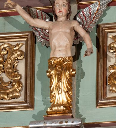 Zdjęcie nr 14: Parapet chóru muzycznego podtrzymywany przez dwie podpory. Balustrada na cokole, podzielona na cztery pola, wydzielone czterema pilastrami o trzonach w formie spływów wolutowych dekorowanych kampanulami i środkową hermą z półpostacią anioła. Pilastry podtrzymują niepełne belkowanie wyłamane na ich osi. Na belkowaniu, na osi skrajnych pilastrów wazony z kwiatami. W polach płyciny w formie leżącego prostokąta, ujęte profilowanymi ramami. W dwóch skrajnych płycinach przedstawienia instrumentów muzycznych ujętych rocaille'm. Dwie środkowe płyciny z figurkami muzykujących puttów flankowanych rocaille'm. Dolna krawędź balustrady, na osi środkowej dekorowana dwiema stykającymi się wolutami, przechodzącymi we wstęgę, ozdobioną rocaille'm. Balustrada polichromowana w kolorze seledynowym, z kolorowymi profilami, ornamentyka i spływy wolutowe złocone i srebrzone. 


