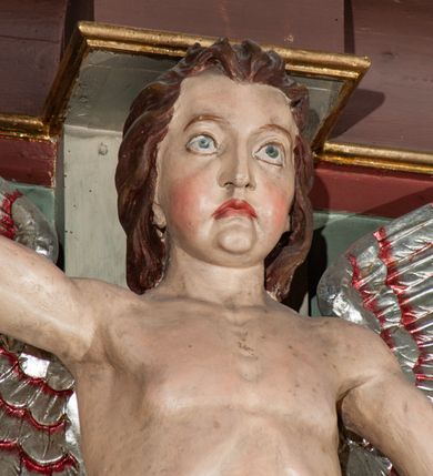 Zdjęcie nr 17: Parapet chóru muzycznego podtrzymywany przez dwie podpory. Balustrada na cokole, podzielona na cztery pola, wydzielone czterema pilastrami o trzonach w formie spływów wolutowych dekorowanych kampanulami i środkową hermą z półpostacią anioła. Pilastry podtrzymują niepełne belkowanie wyłamane na ich osi. Na belkowaniu, na osi skrajnych pilastrów wazony z kwiatami. W polach płyciny w formie leżącego prostokąta, ujęte profilowanymi ramami. W dwóch skrajnych płycinach przedstawienia instrumentów muzycznych ujętych rocaille'm. Dwie środkowe płyciny z figurkami muzykujących puttów flankowanych rocaille'm. Dolna krawędź balustrady, na osi środkowej dekorowana dwiema stykającymi się wolutami, przechodzącymi we wstęgę, ozdobioną rocaille'm. Balustrada polichromowana w kolorze seledynowym, z kolorowymi profilami, ornamentyka i spływy wolutowe złocone i srebrzone. 


