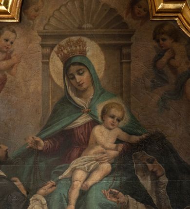 Zdjęcie nr 4: Obraz w formie stojącego prostokąta zamkniętego łukiem półkolistym nadwieszonym z uskokiem. W centrum ukazana Matka Boska siedząca na tronie z wysokim zapleckiem, zwieńczonym palmetą, ustawionym na dwustopniowej podstawie, flankowana przez klęczące poniżej postacie św. Dominika i św. Katarzyny Sieneńskiej. Maria ukazana frontalnie, z głową przechyloną na prawe ramię, lewą ręką przytrzymuje siedzące na jej kolanach Dzieciątko, prawą wyciąga w bok podając różaniec św. Dominikowi. Twarz ma owalną, o dużych oczach skierowanych w dół, prostym nosie i małych ustach, okoloną włosami ukrytymi pod welonem. Ubrana jest w blado czerwoną suknię, przepasaną w talii, wokół głowy i szyi ma białą podwikę, na głowę i ramiona ma narzucony jasnoniebieski płaszcz, zapięty klamrą pod szyją i opadający na kolana. Na głowie ma koronę otwartą, wokół niej nimb. Dzieciątko ukazane w pozycji siedzącej, frontalnie, przechylone w lewo, z wyciągniętymi w bok rekami, z których lewą kładzie na głowie św. Katarzyny, a prawą podaje jej różaniec. Twarz ma pełną, o dużych oczach, małym nosie i ustach, okoloną krótkimi, jasnymi włosami. Przez biodra ma przewiązaną białą pieluszkę. Wokół głowy ma kwadratowy nimb. W lewej części obrazu ukazana klęcząca postać św. Dominika zwróconego profilem w lewo, z uniesioną głową, prawą wyciągniętą ręką odbiera różaniec, lewą kładzie na piersi. Twarz ma szczupłą, o dużych oczach skierowanych w górę, prostym nosie i małych ustach, okoloną krótką brodą i włosami, z tonsurą na głowie. Ubrany jest w biały, luźny habit ze szkaplerzem i czarny płaszcz z pelerynką i kapturem. Nad głową ma aureolę. W prawej części obrazu ukazana klęcząca św. Katarzyna, zwrócona profilem w prawo, z pochyloną głową, prawą wyciągniętą ręką odbiera różaniec, lewą ma opuszczoną.  Twarz ma szczupłą, o oczach skierowanych w dół, prostym nosie i małych ustach. Ubrana jest w biały, luźny habit ze szkaplerzem, wokół twarzy ma białą podwikę, na plecy ma narzucony czarny płaszcz, na głowie zaś czarny welon i koronę cierniową, ponad nią aureolę. W dolnej części obrazu, na stopniu, pomiędzy świętymi leżą dwie gałązki lilii i różany wieniec. Postacie ukazane na tle błękitno-różowego nieba, wypełnionego obłokami z postaciami unoszących się dwóch puttów flankujących tron i trzech uskrzydlonych główek anielskich ponad nim. 
