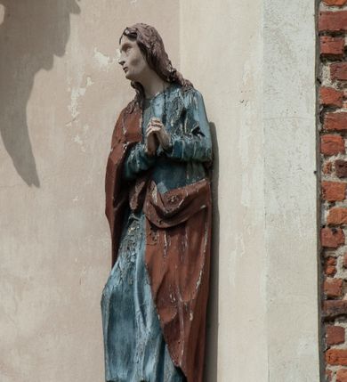 Zdjęcie nr 8: Grupa rzeźbiarska umieszczona we wnęce w formie stojącego prostokąta zamkniętego łukiem półkolistym. W centrum krzyż wypełniający całą wnękę, osadzony na skale, do którego trzema gwoździami przybita jest figura umarłego Chrystusa. Ciało ma w lekkim zwisie, o horyzontalnie rozłożonych ramionach, jego głowa opada na prawy bark, nogi ma lekko ugięte w kolanach, a stopy skrzyżowane w układzie prawa na lewą. Twarz ma szczupłą, o zamkniętych oczach, dużym nosie i otwartych ustach, okoloną krótką, kręconą brodą oraz falowanymi, brązowymi włosami, opadającymi na prawe ramię. Na głowie ma szeroką, brązową koronę cierniową. Ciało o lekko podkreślonej muskulaturze i silnie zaznaczonych żebrach klatki piersiowej. Przez biodra przewiązane krótkie, białe perizonium ze zwisem tkaniny na prawym boku. 
Po lewej stronie krzyża figura Marii, ustawiona na półkolistej podstawie. Matka Boska zwrócona w trzech czwartych w lewo, z pochyloną głową oraz rękami skrzyżowanymi na piersi. Twarz ma owalną, o dużych, migdałowatych oczach, dużym nosie i wąskich ustach. Ubrana jest w białą suknię oraz jasnoniebieski płaszcz z szerokimi rękawami, rozchylony z przodu, na głowę ma narzucony biały welon opadający na ramiona. 
Po prawej stronie krzyża figura św. Jana ustawiona na półkolistej podstawie. Święty zwrócony w trzech czwartych w prawo, w kontrapoście, z uniesionymi, splecionymi dłońmi. Twarz ma szczupłą, o migdałowatych oczach, prostym nosie i wąskich ustach, okoloną gęstymi, kręconymi, brązowymi włosami, opadającymi na ramiona. Ubrany jest w jasnoniebieską suknię oraz zawiązany diagonalnie przez prawe ramię czerwony płaszcz. Polichromia ciał naturalistyczna. 
