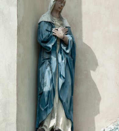 Zdjęcie nr 6: Grupa rzeźbiarska umieszczona we wnęce w formie stojącego prostokąta zamkniętego łukiem półkolistym. W centrum krzyż wypełniający całą wnękę, osadzony na skale, do którego trzema gwoździami przybita jest figura umarłego Chrystusa. Ciało ma w lekkim zwisie, o horyzontalnie rozłożonych ramionach, jego głowa opada na prawy bark, nogi ma lekko ugięte w kolanach, a stopy skrzyżowane w układzie prawa na lewą. Twarz ma szczupłą, o zamkniętych oczach, dużym nosie i otwartych ustach, okoloną krótką, kręconą brodą oraz falowanymi, brązowymi włosami, opadającymi na prawe ramię. Na głowie ma szeroką, brązową koronę cierniową. Ciało o lekko podkreślonej muskulaturze i silnie zaznaczonych żebrach klatki piersiowej. Przez biodra przewiązane krótkie, białe perizonium ze zwisem tkaniny na prawym boku. 
Po lewej stronie krzyża figura Marii, ustawiona na półkolistej podstawie. Matka Boska zwrócona w trzech czwartych w lewo, z pochyloną głową oraz rękami skrzyżowanymi na piersi. Twarz ma owalną, o dużych, migdałowatych oczach, dużym nosie i wąskich ustach. Ubrana jest w białą suknię oraz jasnoniebieski płaszcz z szerokimi rękawami, rozchylony z przodu, na głowę ma narzucony biały welon opadający na ramiona. 
Po prawej stronie krzyża figura św. Jana ustawiona na półkolistej podstawie. Święty zwrócony w trzech czwartych w prawo, w kontrapoście, z uniesionymi, splecionymi dłońmi. Twarz ma szczupłą, o migdałowatych oczach, prostym nosie i wąskich ustach, okoloną gęstymi, kręconymi, brązowymi włosami, opadającymi na ramiona. Ubrany jest w jasnoniebieską suknię oraz zawiązany diagonalnie przez prawe ramię czerwony płaszcz. Polichromia ciał naturalistyczna. 
