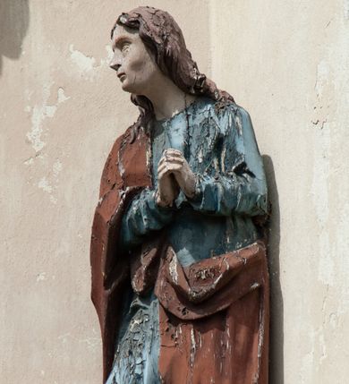 Zdjęcie nr 9: Grupa rzeźbiarska umieszczona we wnęce w formie stojącego prostokąta zamkniętego łukiem półkolistym. W centrum krzyż wypełniający całą wnękę, osadzony na skale, do którego trzema gwoździami przybita jest figura umarłego Chrystusa. Ciało ma w lekkim zwisie, o horyzontalnie rozłożonych ramionach, jego głowa opada na prawy bark, nogi ma lekko ugięte w kolanach, a stopy skrzyżowane w układzie prawa na lewą. Twarz ma szczupłą, o zamkniętych oczach, dużym nosie i otwartych ustach, okoloną krótką, kręconą brodą oraz falowanymi, brązowymi włosami, opadającymi na prawe ramię. Na głowie ma szeroką, brązową koronę cierniową. Ciało o lekko podkreślonej muskulaturze i silnie zaznaczonych żebrach klatki piersiowej. Przez biodra przewiązane krótkie, białe perizonium ze zwisem tkaniny na prawym boku. 
Po lewej stronie krzyża figura Marii, ustawiona na półkolistej podstawie. Matka Boska zwrócona w trzech czwartych w lewo, z pochyloną głową oraz rękami skrzyżowanymi na piersi. Twarz ma owalną, o dużych, migdałowatych oczach, dużym nosie i wąskich ustach. Ubrana jest w białą suknię oraz jasnoniebieski płaszcz z szerokimi rękawami, rozchylony z przodu, na głowę ma narzucony biały welon opadający na ramiona. 
Po prawej stronie krzyża figura św. Jana ustawiona na półkolistej podstawie. Święty zwrócony w trzech czwartych w prawo, w kontrapoście, z uniesionymi, splecionymi dłońmi. Twarz ma szczupłą, o migdałowatych oczach, prostym nosie i wąskich ustach, okoloną gęstymi, kręconymi, brązowymi włosami, opadającymi na ramiona. Ubrany jest w jasnoniebieską suknię oraz zawiązany diagonalnie przez prawe ramię czerwony płaszcz. Polichromia ciał naturalistyczna. 

