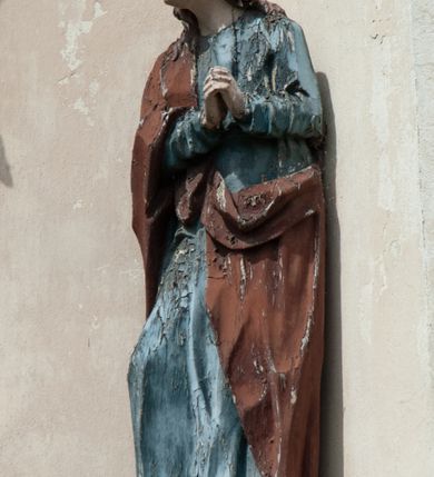 Zdjęcie nr 10: Grupa rzeźbiarska umieszczona we wnęce w formie stojącego prostokąta zamkniętego łukiem półkolistym. W centrum krzyż wypełniający całą wnękę, osadzony na skale, do którego trzema gwoździami przybita jest figura umarłego Chrystusa. Ciało ma w lekkim zwisie, o horyzontalnie rozłożonych ramionach, jego głowa opada na prawy bark, nogi ma lekko ugięte w kolanach, a stopy skrzyżowane w układzie prawa na lewą. Twarz ma szczupłą, o zamkniętych oczach, dużym nosie i otwartych ustach, okoloną krótką, kręconą brodą oraz falowanymi, brązowymi włosami, opadającymi na prawe ramię. Na głowie ma szeroką, brązową koronę cierniową. Ciało o lekko podkreślonej muskulaturze i silnie zaznaczonych żebrach klatki piersiowej. Przez biodra przewiązane krótkie, białe perizonium ze zwisem tkaniny na prawym boku. 
Po lewej stronie krzyża figura Marii, ustawiona na półkolistej podstawie. Matka Boska zwrócona w trzech czwartych w lewo, z pochyloną głową oraz rękami skrzyżowanymi na piersi. Twarz ma owalną, o dużych, migdałowatych oczach, dużym nosie i wąskich ustach. Ubrana jest w białą suknię oraz jasnoniebieski płaszcz z szerokimi rękawami, rozchylony z przodu, na głowę ma narzucony biały welon opadający na ramiona. 
Po prawej stronie krzyża figura św. Jana ustawiona na półkolistej podstawie. Święty zwrócony w trzech czwartych w prawo, w kontrapoście, z uniesionymi, splecionymi dłońmi. Twarz ma szczupłą, o migdałowatych oczach, prostym nosie i wąskich ustach, okoloną gęstymi, kręconymi, brązowymi włosami, opadającymi na ramiona. Ubrany jest w jasnoniebieską suknię oraz zawiązany diagonalnie przez prawe ramię czerwony płaszcz. Polichromia ciał naturalistyczna. 
